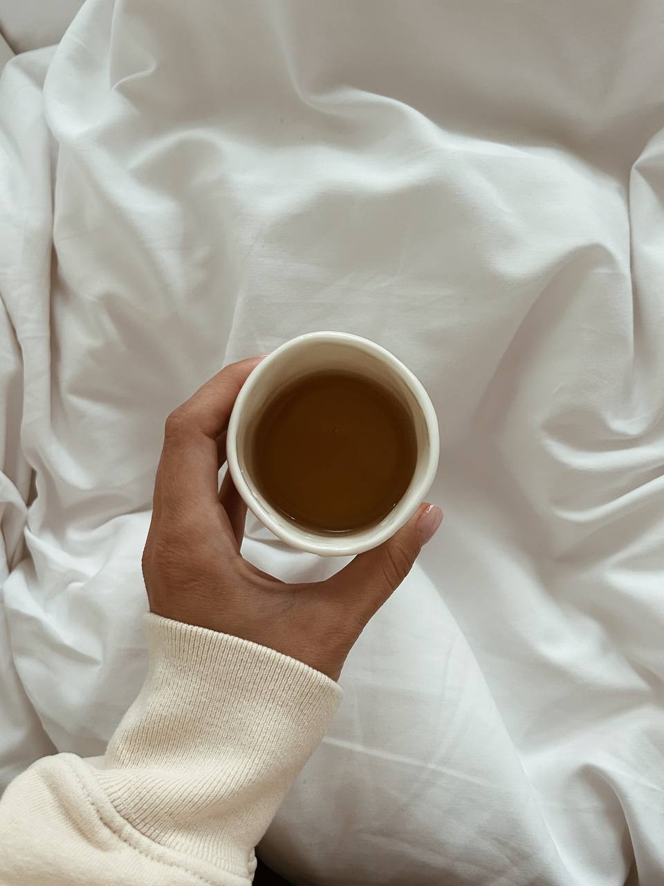 A hand holding a cup of coffee on white sheets