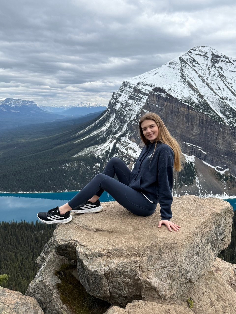 Sia sitting on a rock above a turquoise mountain lake